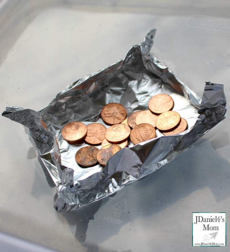 A rectangular tinfoil raft that holds several pennies in it. The raft floats in a container of water.