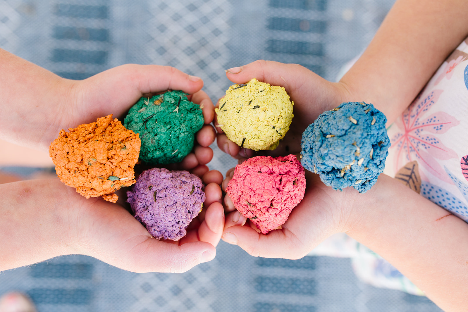 Small hands holding out six colorful seed bombs made out of recycled paper.