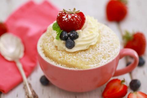 A microwave sponge cake topped with whipped cream and fruit in a pink mug.