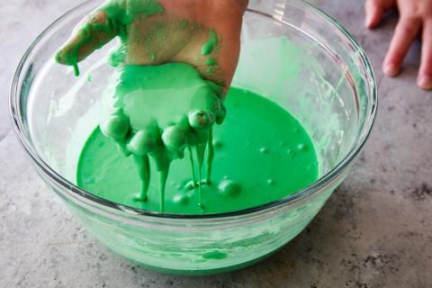 Green oobleck-based slime in a clear glass bowl.