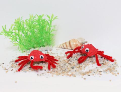 Two craft crabs made with red painted shells, googly eyes, and pipe cleaners.