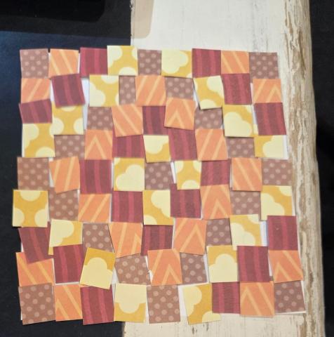 A quilt of paper squares in red, pink, brown, and yellow.